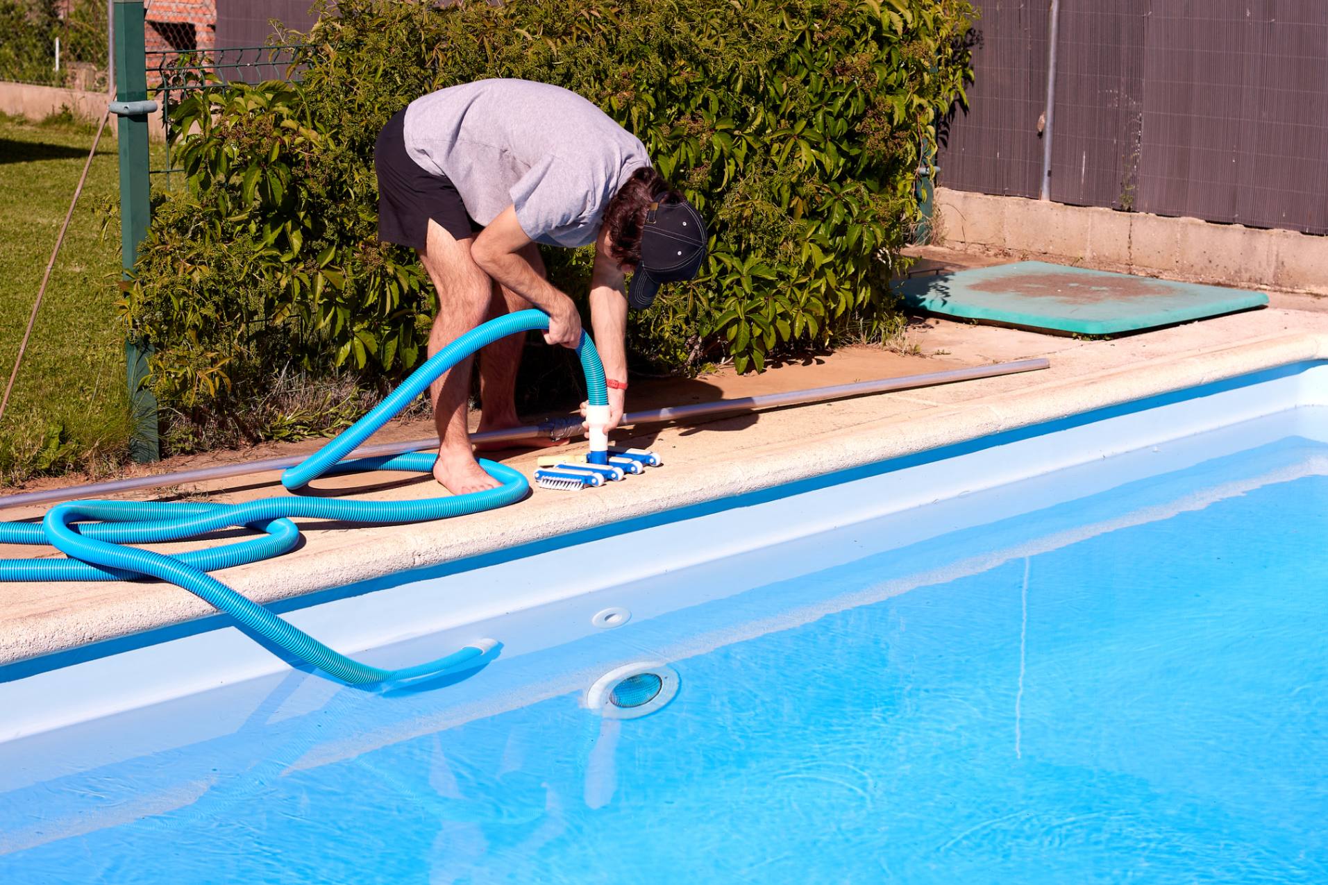 Person cleaning swimming pool with vacuum hose.