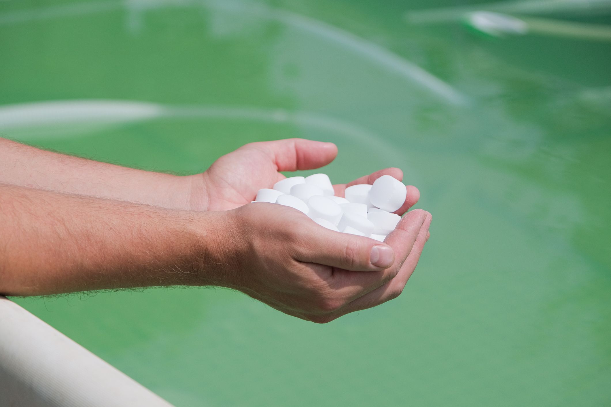 Hands holding white tablets over water.